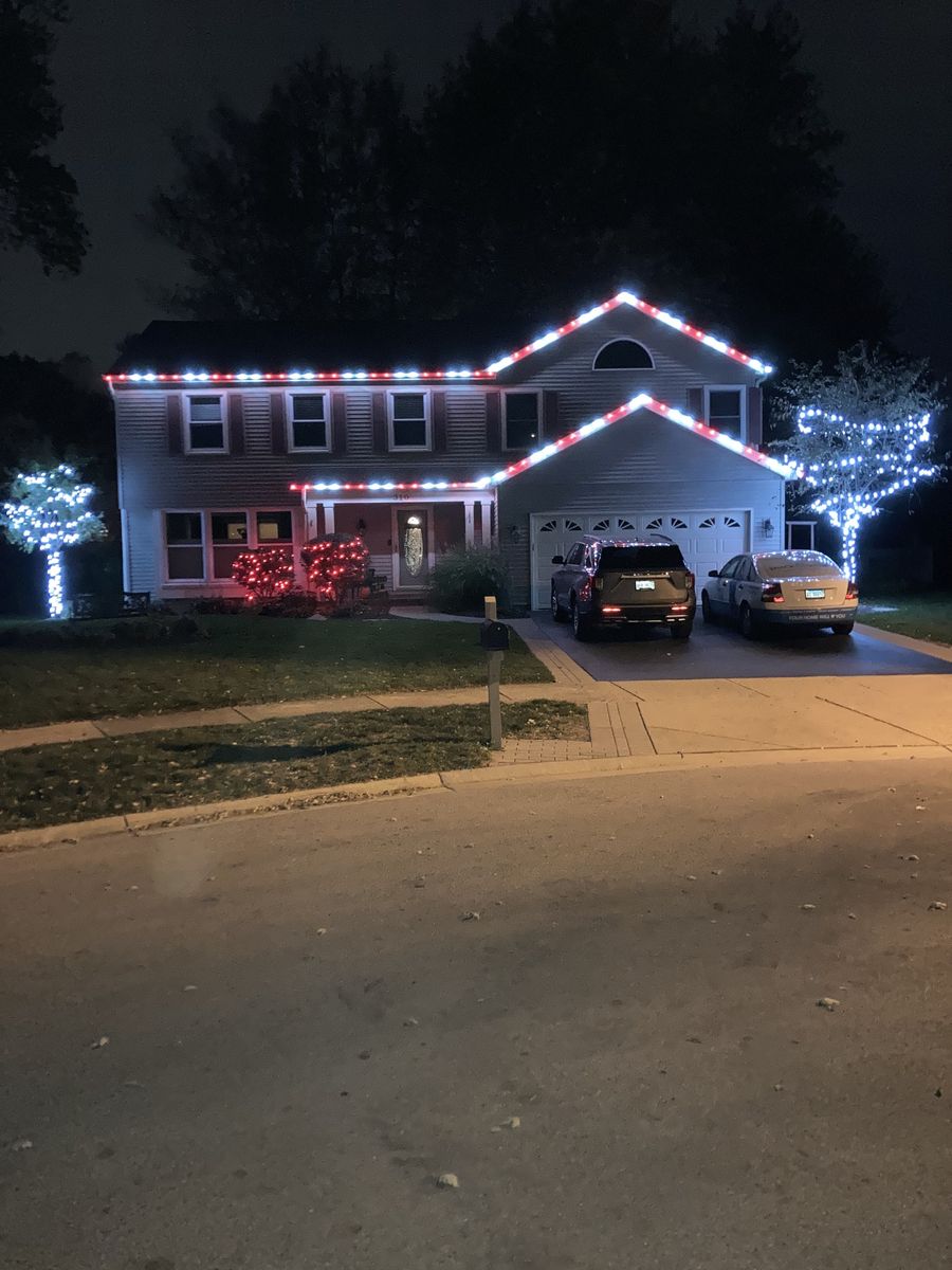 Two-story home with white and red roofline and lit trees