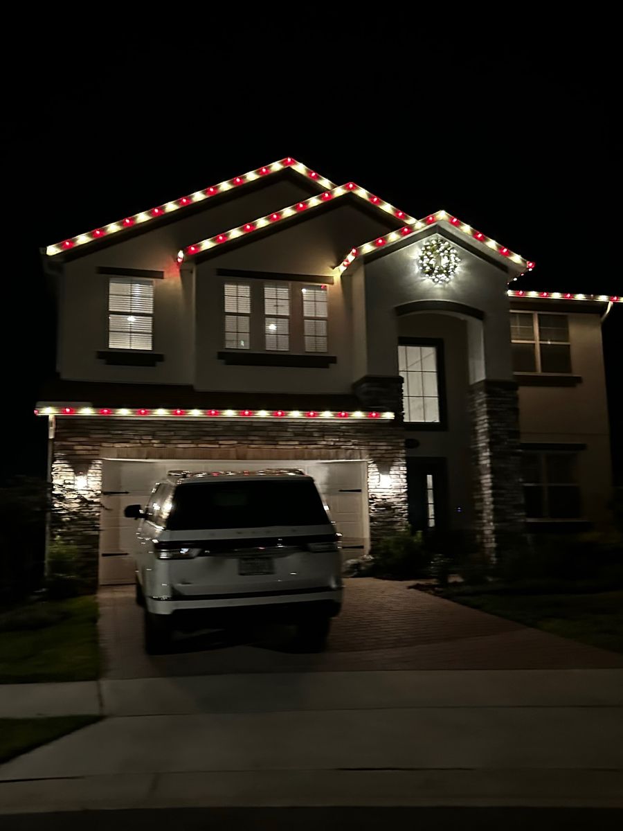 Two-story home with warm white roofline lights and a lit wreath